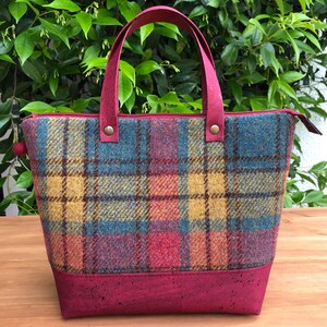 May include: A red, yellow, and blue plaid tote bag with a cork bottom and leather handles.