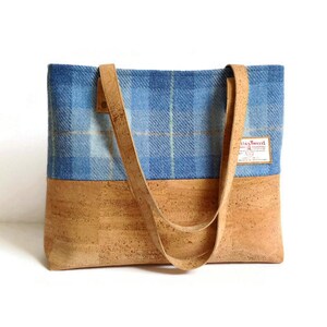 May include: A blue and tan plaid tote bag with cork bottom and leather straps. The bag has a label that says "Harris Tweed".