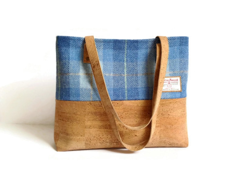 May include: A blue and tan plaid tote bag with cork bottom and leather straps. The bag has a label that says "Harris Tweed".
