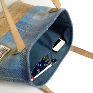 May include: A blue and brown tote bag with a cork handle and a blue tweed fabric body. The bag has a zipper closure and a small pocket on the inside. The bag is open and you can see a phone and a notebook inside.