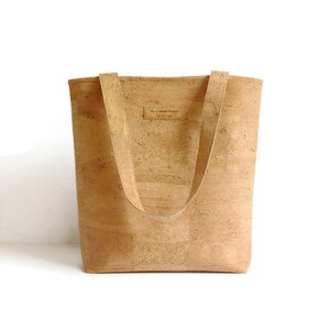 May include: A light brown cork tote bag with two straps. The bag has a small label that says "My Cotton House" on the front.