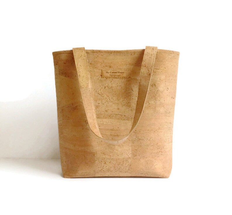 May include: A light brown cork tote bag with two straps. The bag has a small label that says "My Cotton House" on the front.