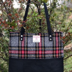 May include: A black tote bag with black straps and a gray and red plaid fabric top. The fabric has a label that reads "Harris Tweed" with the text "100% Pure New Wool" underneath.