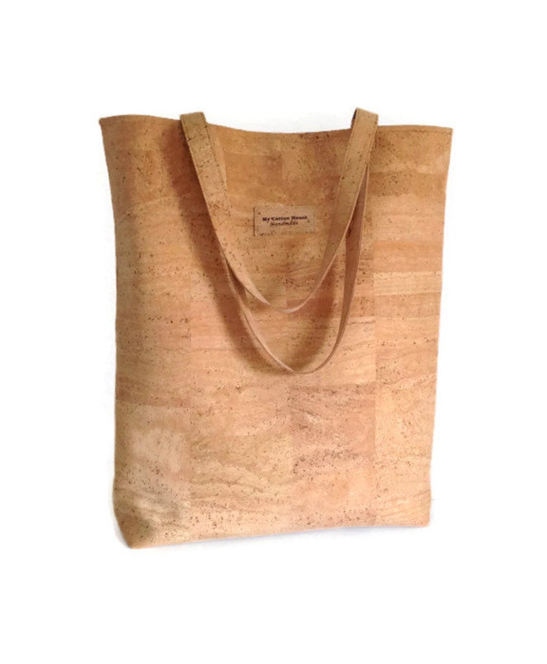 May include: A light brown cork tote bag with two long straps. The bag has a small label that says "My Cotton House Handmade".