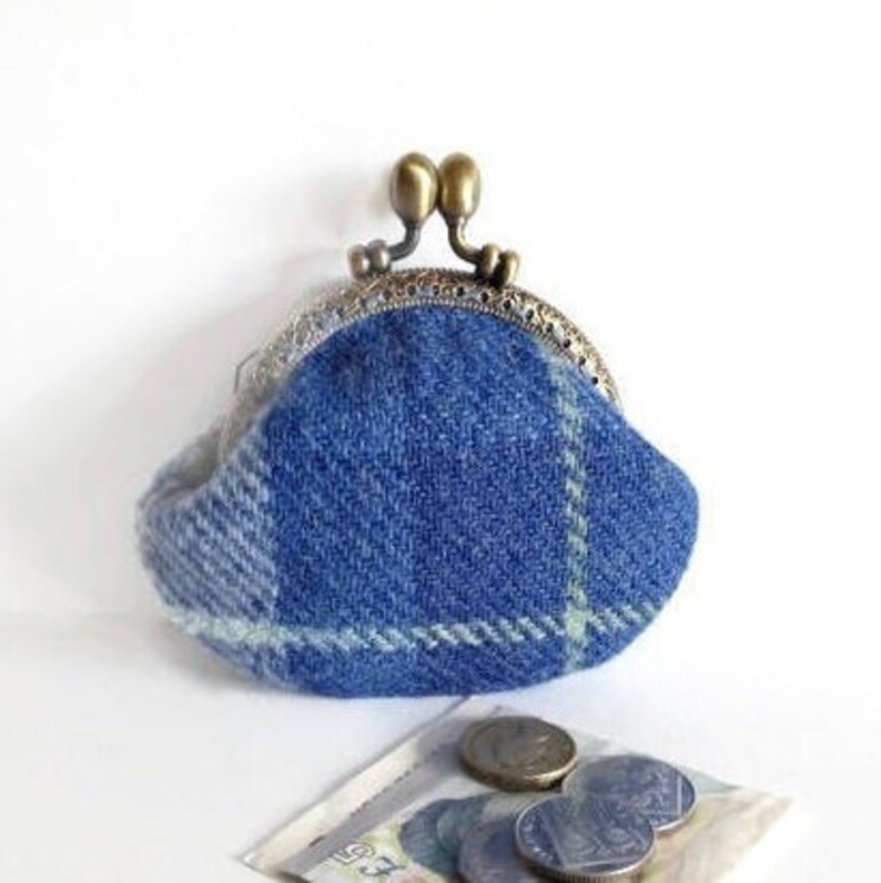 May include: A blue plaid coin purse with a metal clasp. The purse is made of a woven fabric with a blue and white plaid pattern. Several coins and a paper bill are visible near the purse.