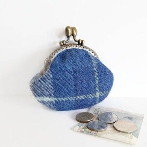 May include: A blue plaid coin purse with a metal clasp, featuring a brass-colored closure. The purse is made of a textured fabric and is accompanied by several coins and a small bill.