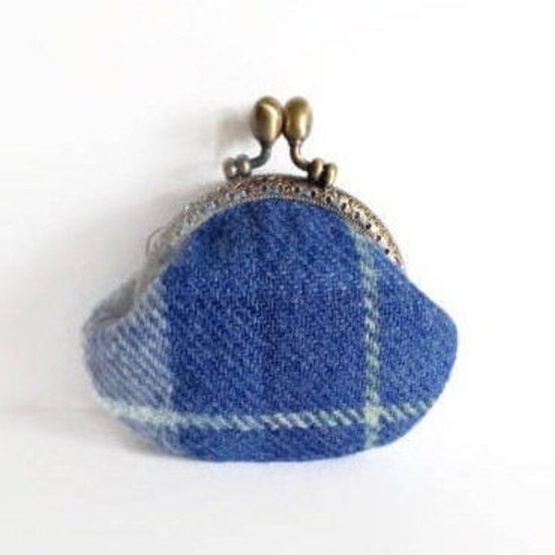 May include: A small, blue plaid coin purse with a metal clasp. The purse is made of a woven fabric with a pattern of light blue and white lines. The clasp is a bronze color and has a double-ball closure.