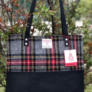 May include: A black tote bag with black straps and a red, yellow, and gray plaid pattern. The bag has a black leather bottom and a label that says "Harris Tweed" with a red and white logo.
