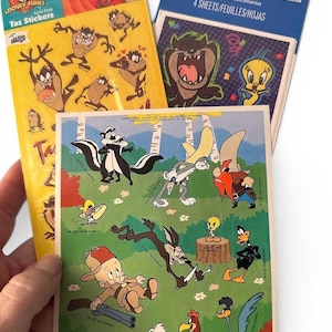 May include: A collection of Looney Tunes stickers featuring characters like Taz, Tweety Bird, and others. The stickers are on yellow and blue packaging, with the words "Tax Stickers" visible. The image also includes a sheet of stickers with various cartoon characters.