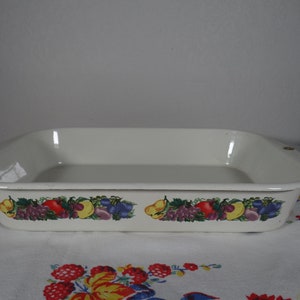 May include: Off-white rectangular baking dish with a colorful fruit border. The border features illustrations of grapes, plums, pears, and other fruits. The dish is made of ceramic or enamel and is likely vintage.