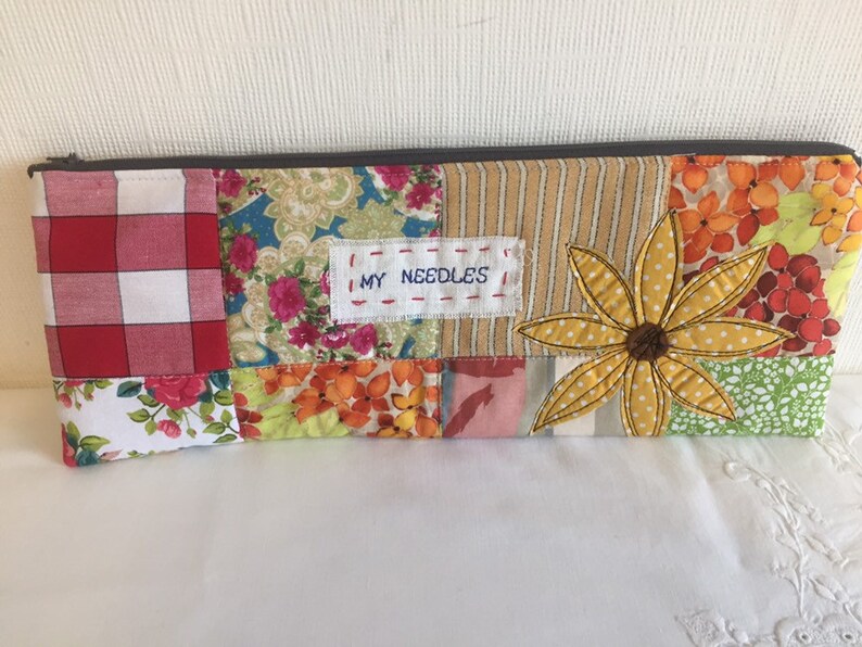 May include: A patchwork fabric zippered pouch with a yellow flower design and the text "MY NEEDLES" on a white label.