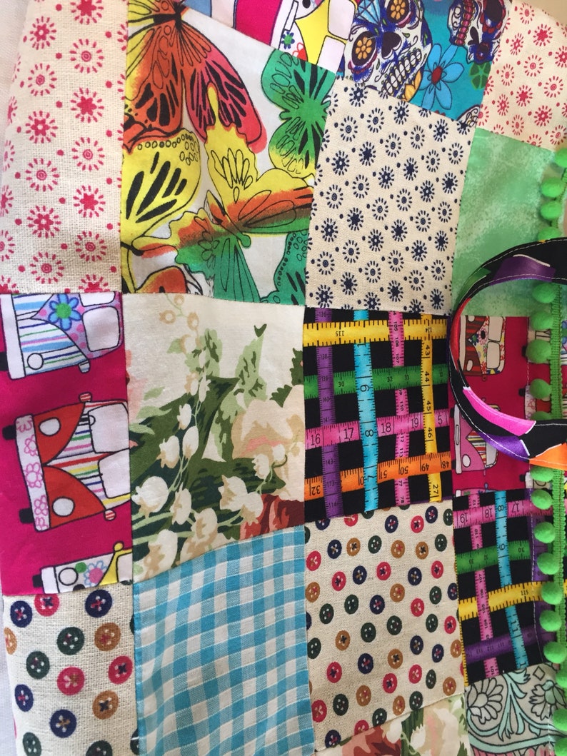 May include: A patchwork fabric bag with a variety of colorful patterns, including butterflies, flowers, and a skull. The bag has a black and white ruler pattern on one side and a green and black striped pattern on the other side.