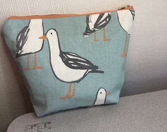 May include: A light blue canvas zippered pouch with a white and black seagull pattern. The pouch has a brown zipper pull.