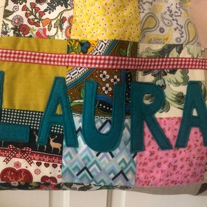 May include: A patchwork fabric tote bag with a red and white gingham ribbon and the name "LAURA" spelled out in teal felt letters.