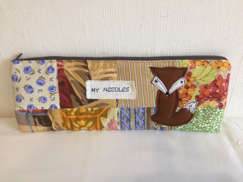 May include: A patchwork fabric zippered pouch with a brown fox applique and the text "MY NEEDLES" on a white label.
