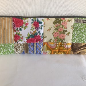 May include: A patchwork fabric zippered pouch with a variety of floral and geometric patterns in shades of green, yellow, pink, blue, and brown. The pouch has a label that reads "Handmade by CraftyHet".