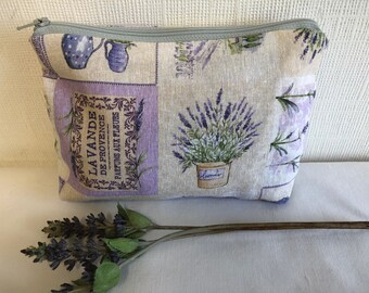 May include: A lavender-themed zippered pouch with a white background and purple accents. The pouch features a repeating pattern of lavender flowers, a pitcher, and a label that reads "LAVANDE DE PROVENCE PARFUMS AUX FLEURS".