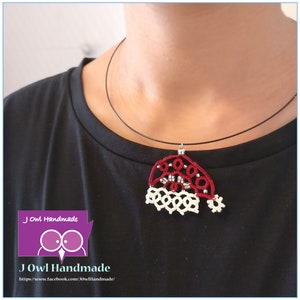 May include: A red and white crocheted Santa hat pendant on a black cord necklace. The pendant is made of delicate, intricate crochet work and features a white pom-pom on top. The necklace is worn by a person with a black shirt.