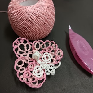 May include: A pink crocheted butterfly with white accents, a ball of pink yarn, and a purple crochet hook.