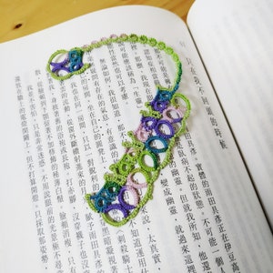 Op de afbeelding: Een groene, paarse en roze gehaakte bladwijzer met een delicaat, ingewikkeld ontwerp. De bladwijzer is in een spiraalvorm gekruld.