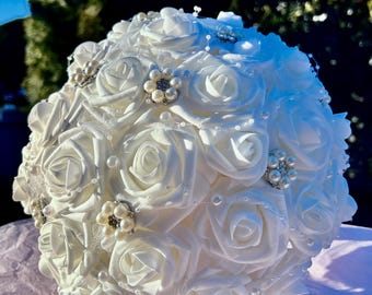 May include: A white bridal bouquet made of artificial roses with pearl and rhinestone embellishments.
