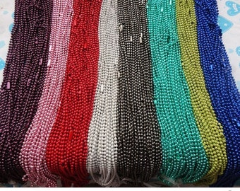 May include: A collection of beaded necklaces in a range of colours: purple, pink, red, white, black, teal, green, and blue. The small beads are evenly spaced, giving a textured look. The necklaces are shown side by side.