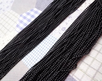 Puede incluir: Primer plano de una gran cantidad de cadena negra, hecha de pequeñas cuentas redondas. La cadena está dispuesta en filas, creando un patrón texturizado.