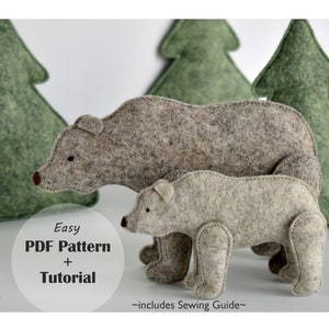 May include: A PDF pattern and tutorial for sewing a brown felt bear and a smaller brown felt bear cub. The bears are standing in front of a green felt forest background. The text "Easy PDF Pattern + Tutorial" is on a white circle. The text "~Includes Sewing Guide~" is below the circle.