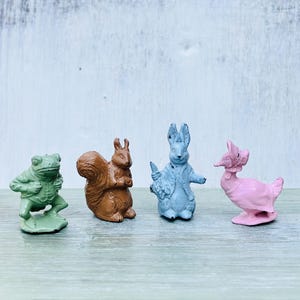 May include: Four small painted figurines of animals. A green frog, a brown squirrel, a blue rabbit, and a pink duck.