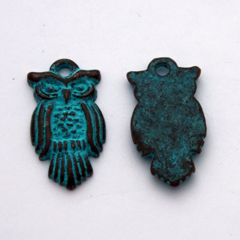 May include: Two turquoise blue metal owl charms with a hole at the top for hanging. The owl on the left has detailed features, while the owl on the right is a silhouette.
