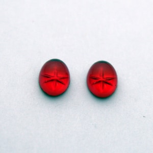 May include: Two red oval-shaped cabochon gemstones with a star-shaped design.