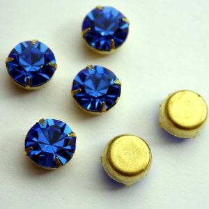 May include: Five blue rhinestones with gold settings and two gold settings without rhinestones.