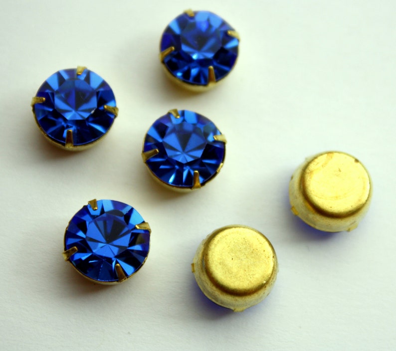 May include: Five blue rhinestones with gold settings and two gold settings without rhinestones.