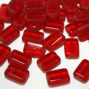 May include: A group of red glass beads, each with a rectangular shape and a slightly translucent appearance.