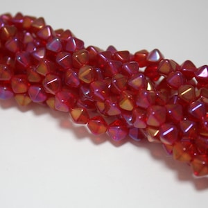 May include: A strand of red iridescent glass beads in a faceted pyramid shape.
