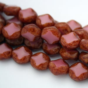 May include: A strand of brown and pink glass beads with a star-shaped design. The beads are faceted and have a mottled brown color with a pink center.