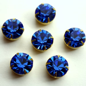 May include: Six blue rhinestones with gold settings. The rhinestones are round and have a faceted design.