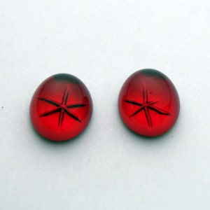 May include: Two red glass cabochons with a star-shaped design.