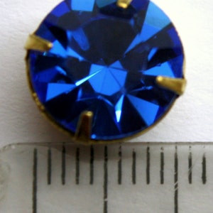 May include: A bright blue rhinestone with gold settings, measuring approximately 1 cm in diameter.