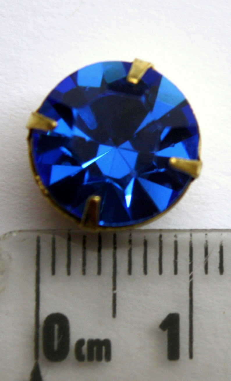 May include: A bright blue rhinestone with gold settings, measuring approximately 1 cm in diameter.