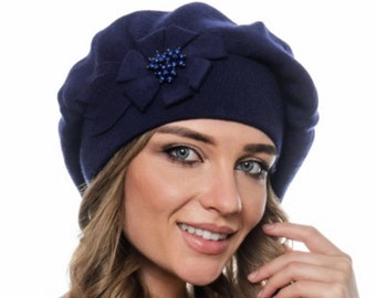 May include: A navy blue beret with a decorative flower and a cluster of small, dark blue beads. The beret is made of a soft, knitted material and is a stylish accessory.