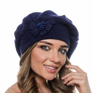 May include: A navy blue beret with a decorative flower and a cluster of small, dark blue beads. The beret is made of a soft, knitted material and is a stylish accessory.