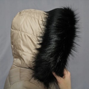 Può includere: Una giacca beige con cappuccio e un bordo in pelliccia sintetica nera intorno al cappuccio.