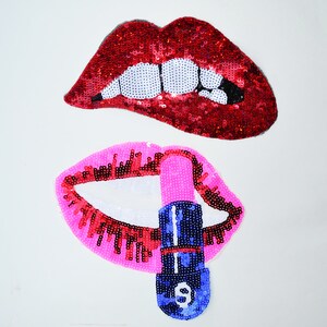Può includere: Due toppe di labbra con paillettes. Una è rossa con denti bianchi e l'altra è rosa con un labbro rosso e un rossetto blu e rosa.
