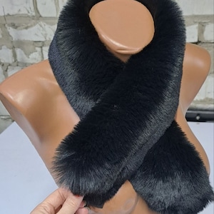 Könnte beinhalten: Ein schwarzer Kunstfell-Halswärmer. Der Halswärmer ist aus weichem, flauschigem Fell gefertigt und soll Sie im Winter warm halten.