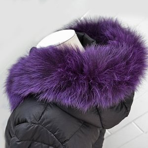 May include: A black puffer jacket with a purple faux fur collar. The collar is thick and fluffy, and it is attached to the jacket with a zipper.