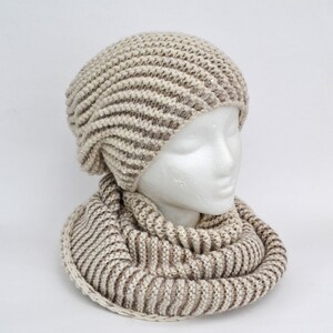 May include: A beige and brown striped knit hat and matching scarf. The hat has a slouchy fit and the scarf is a cowl style.
