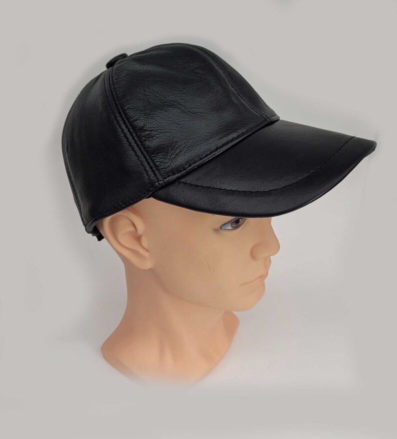 Puede incluir: Una gorra de b&eacute;isbol de cuero negro con visera curva. La gorra se lleva puesta en la cabeza de un maniqu&iacute;.