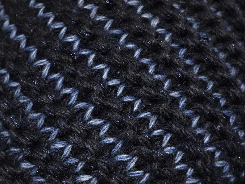 May include: Close-up of a dark blue knitted fabric with a subtle shimmer. The fabric has a textured pattern with a diagonal stitch.