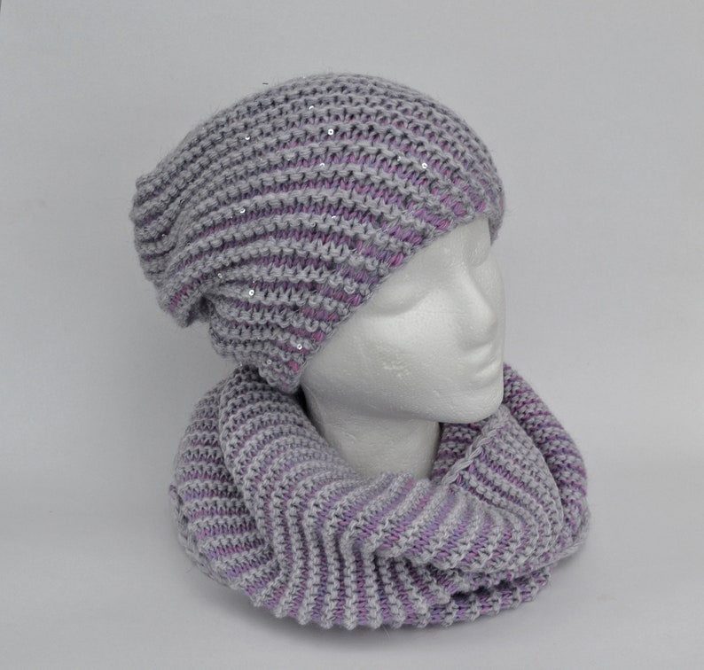 May include: A gray and purple knit beanie with sequins and a matching knit scarf.